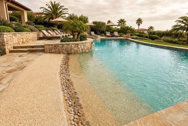 Pebble finish beach entry pool with a textured sandy-toned shallow slope