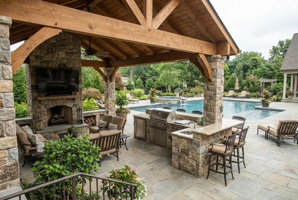 Covered outdoor kitchen and bar with a mounted TV overlooking a pool