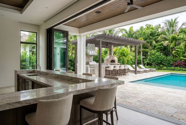 Outdoor kitchen bar overlooking a swimming pool with stools facing the water
