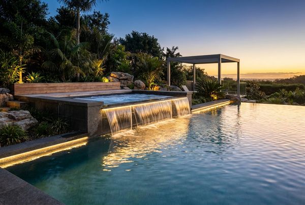 Raised spa spilling into a pool at dusk
