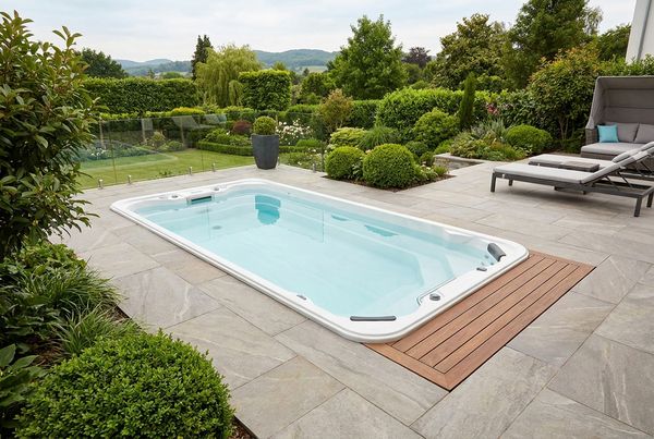 In-ground swim spa set flush into a stone deck in a modern backyard