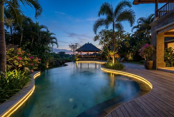 Tropical pool lit warmly at dusk with glowing water and uplit palms