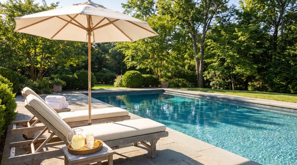 Backyard pool with lounge chairs, umbrella and poolside towels on a sunny day