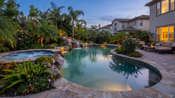 Custom gunite swimming pool with a stone waterfall and raised spa at dusk