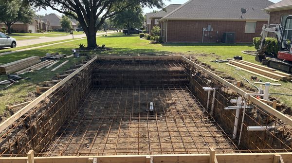 Inground pool under construction with steel rebar shell framing in a backyard