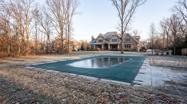 Inground pool secured with a green mesh safety cover on a frosty autumn morning