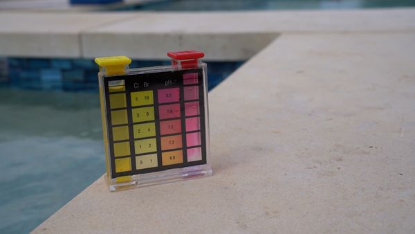 Pool water test kit sitting on the coping beside clear blue water